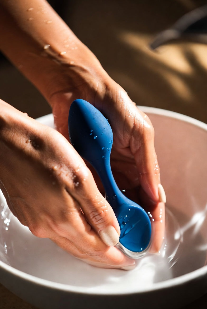 a small silicone toys is being washed by two female hands in a small bowl filled with water