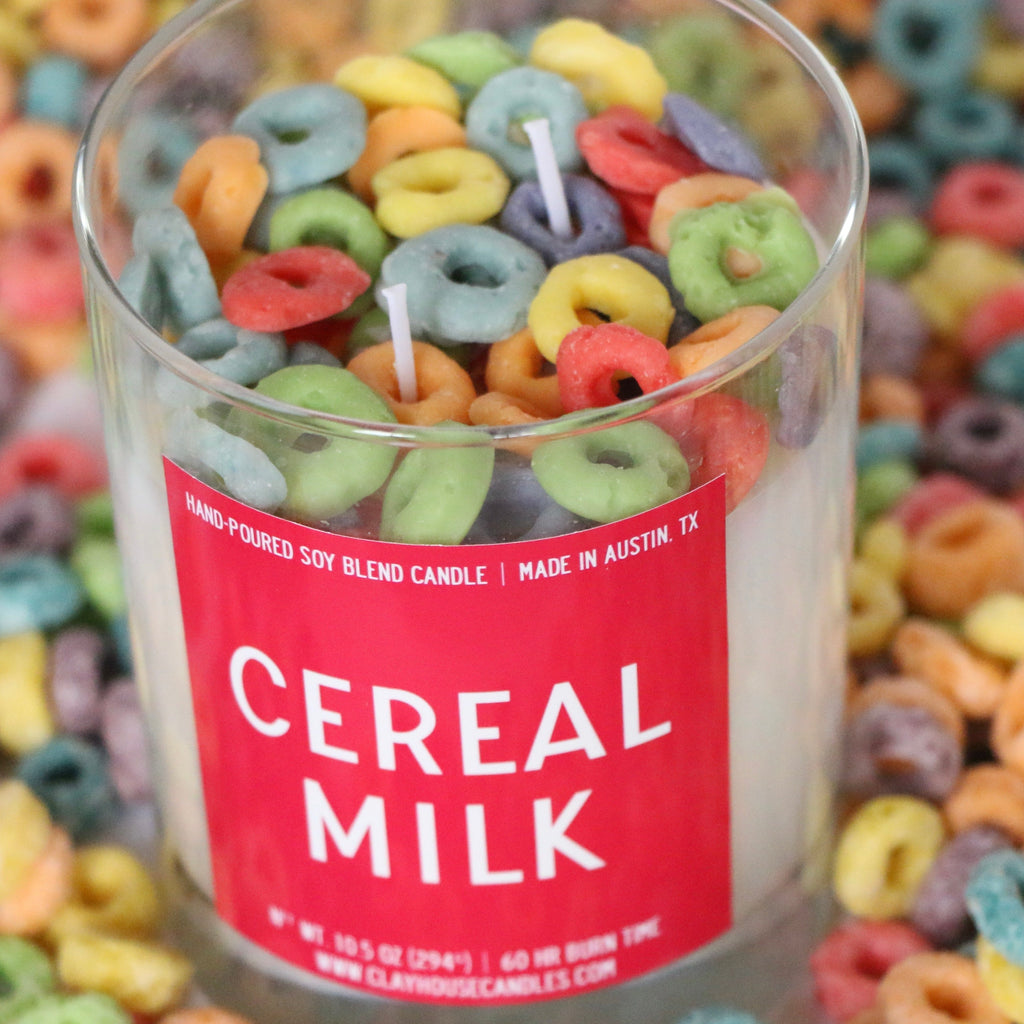 Candle with colorful cereal loops and a 'Cereal Milk' label on a background of cereal loops.