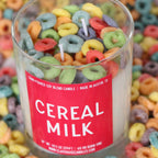 Candle with colorful cereal loops and a 'Cereal Milk' label on a background of cereal loops.