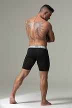 Man wearing black boxer briefs with a visible brand logo on a neutral background