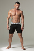 Man wearing black boxer briefs with a gray waistband on a neutral background